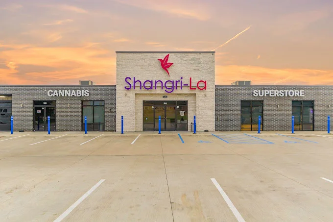 Front view of a Shangri-La Cannabis Superstore building with empty parking spaces at sunset