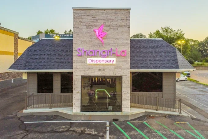 Front view of a small commercial building with a stone facade and a purple 'Shangri-La' sign above the entrance