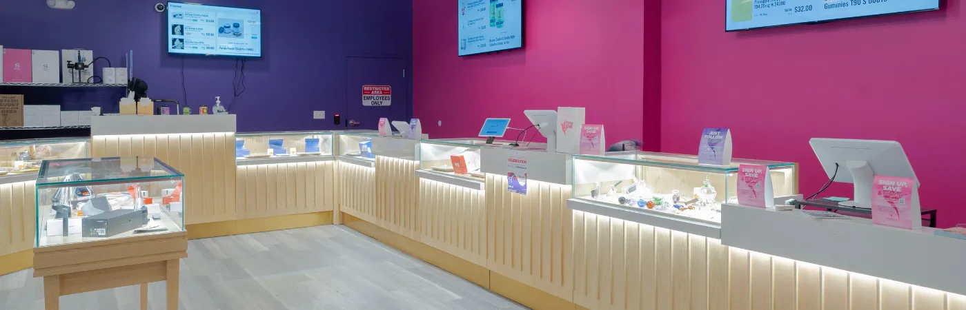 Brightly lit retail store interior with glass display cases showcasing various products against vibrant purple and pink walls